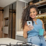 Mulher em uma cozinha com celular e caneca de café na mão