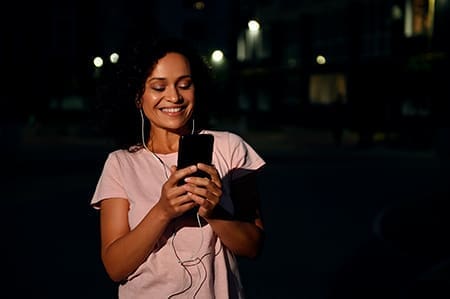 Foto de mulher usando fone de ouvido conectado ao celular a noite