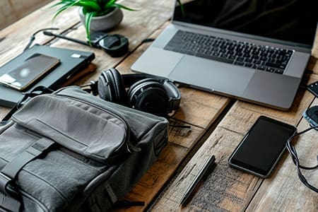 Mesa de trabalho com notebook, celular e fone de ouvido.